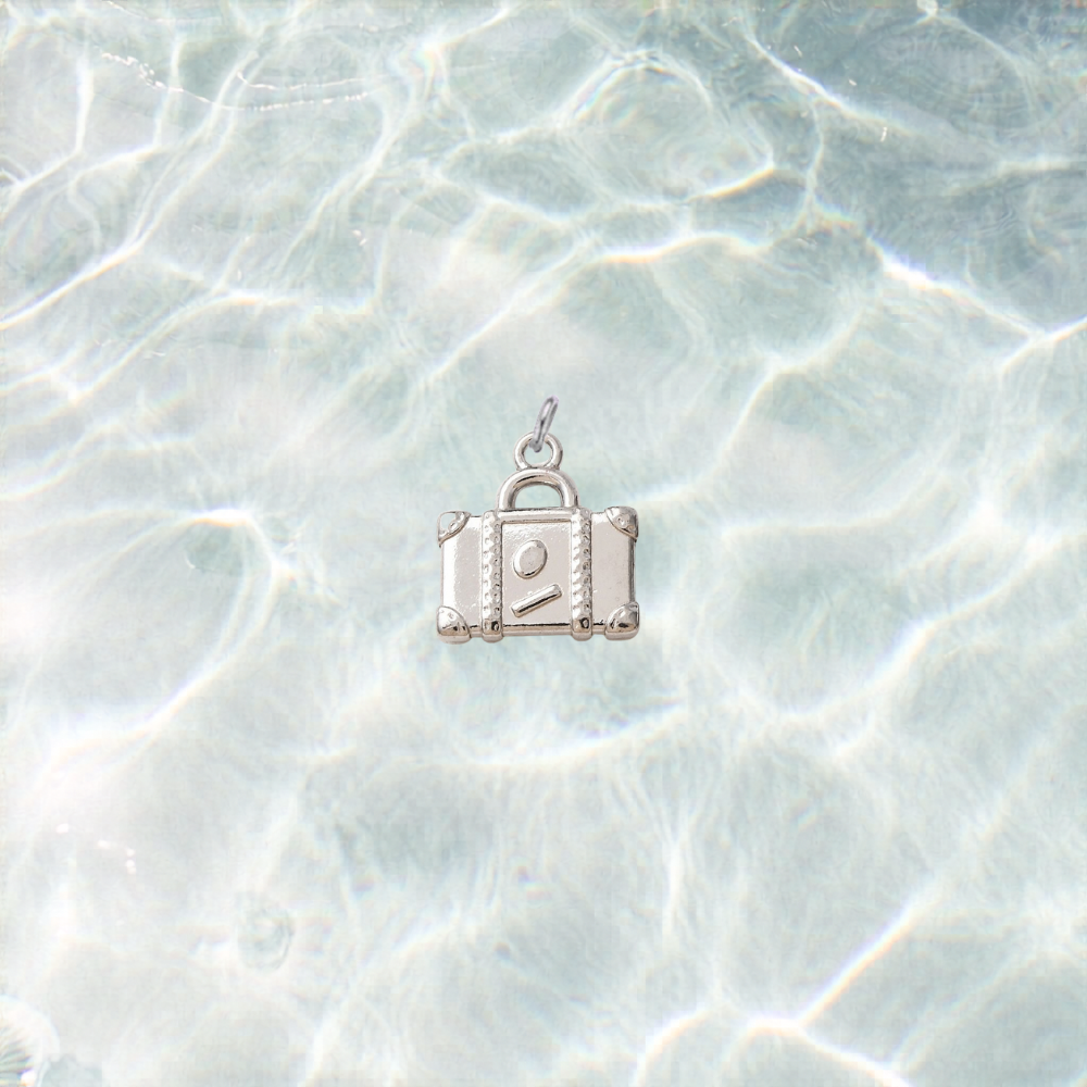 Silver waterproof suitcase charm with a polished finish on a shimmering light blue water background.