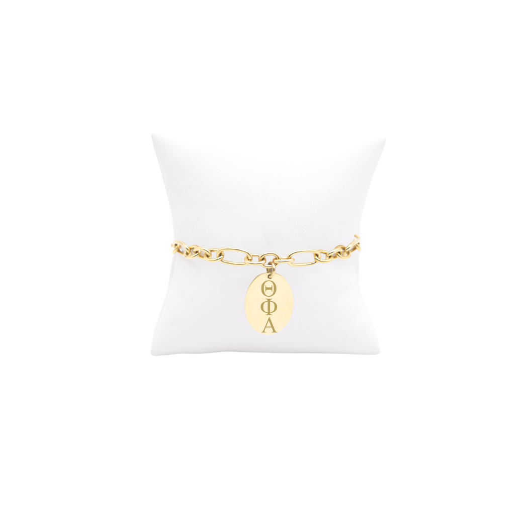 Theta Phi Alpha gold large link keepsake bracelet with large oval charm displayed on white pillow front view with horizontal greek letters